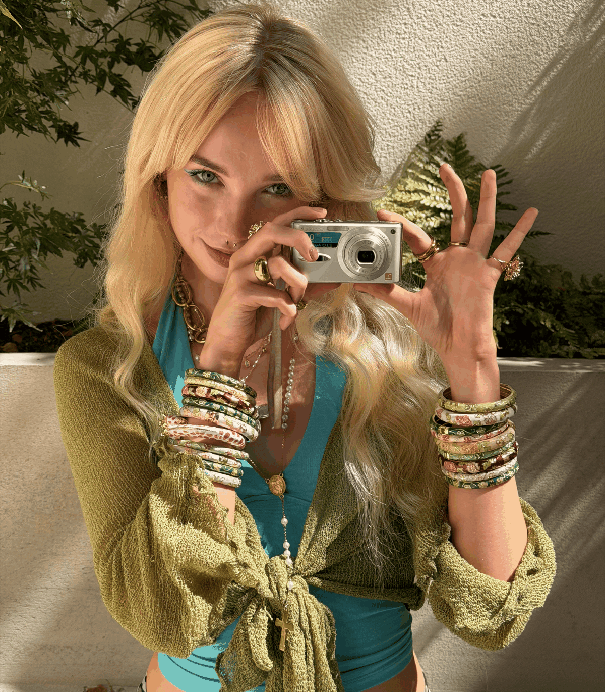 welcome to the STAR GIRL DIARIES ★ fashion portrait of a blonde woman in a turquoise top and green knit wrap, holding a silver compact camera