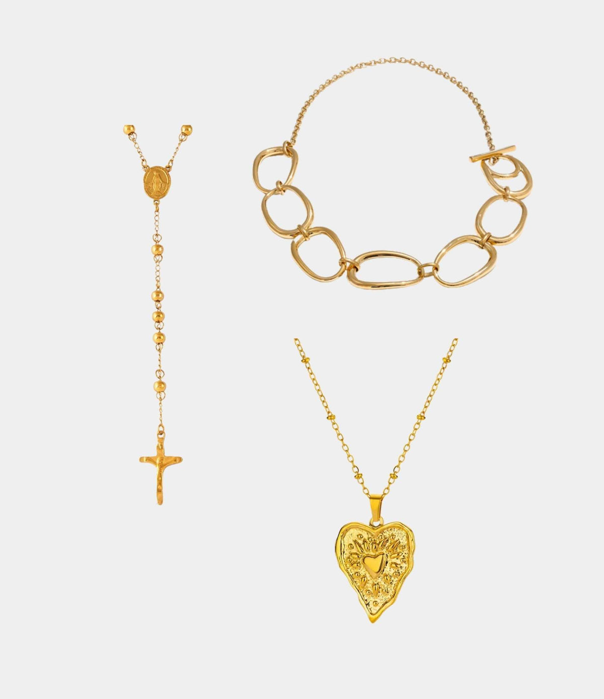 THE ICON NECKLACE SET features three gold-tone necklaces: oval links, a beaded cross pendant, and an ornate heart pendant.