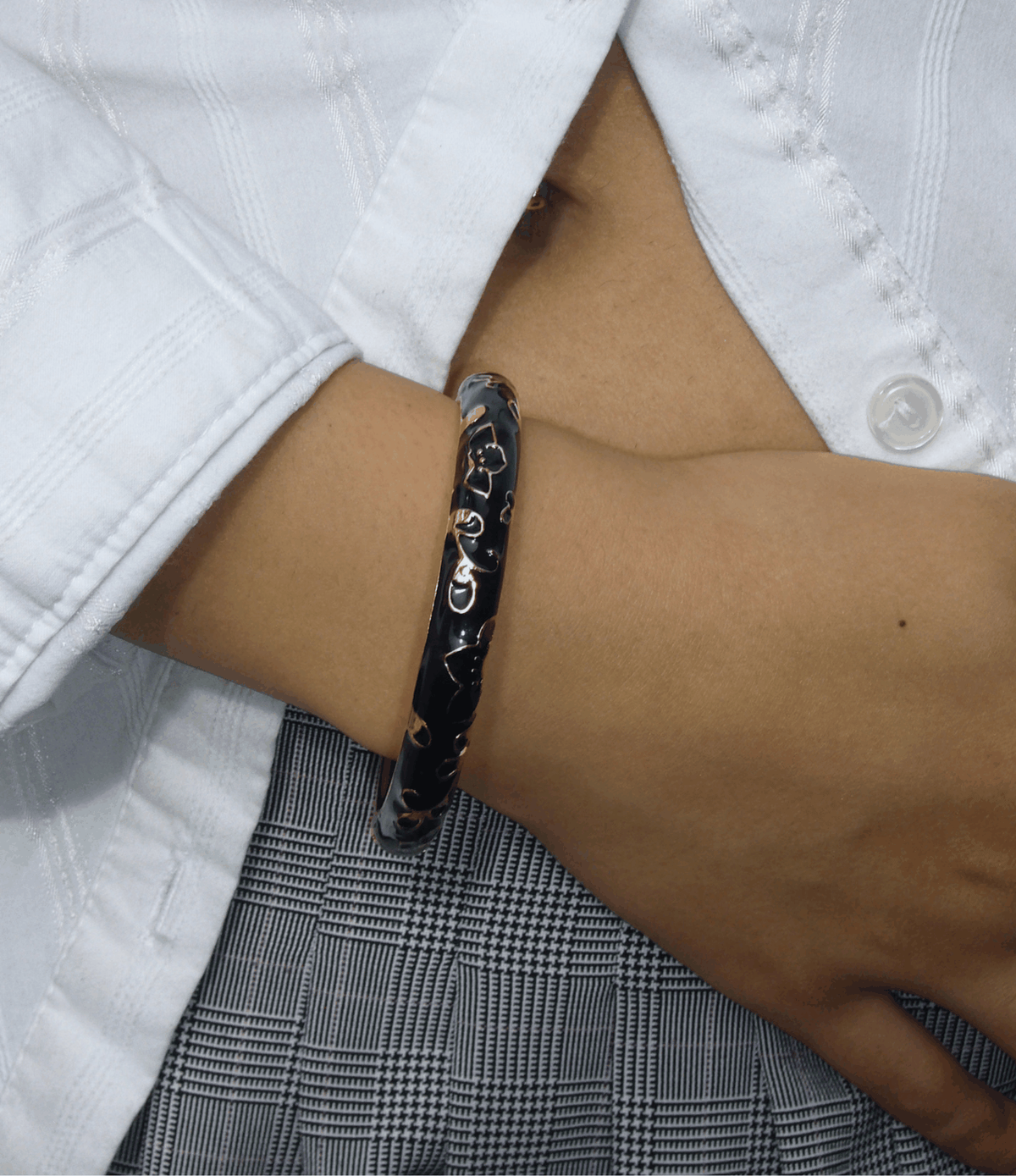 DAHLIA BANGLE IN BLACK, a glossy black enamel bangle with a curved openwork pattern and gold-toned accents