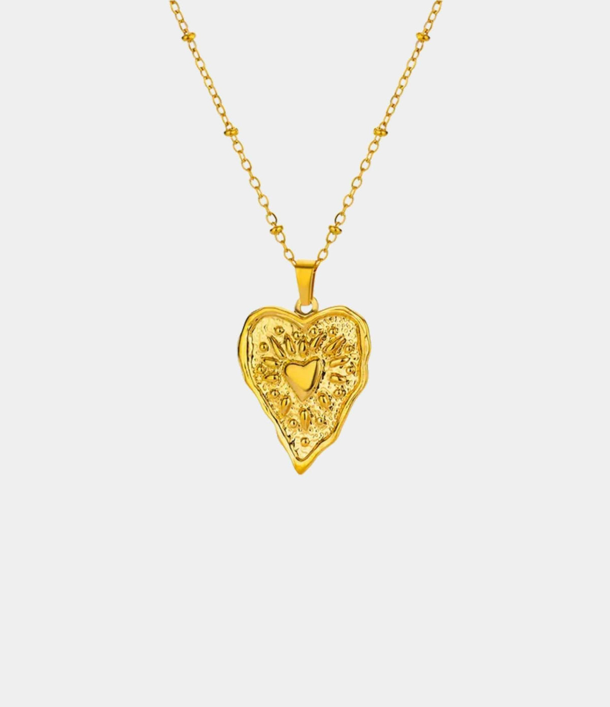 Gold-tone GRACE NECKLACE with a fine chain and ornate heart-shaped pendant featuring a small raised heart detail.