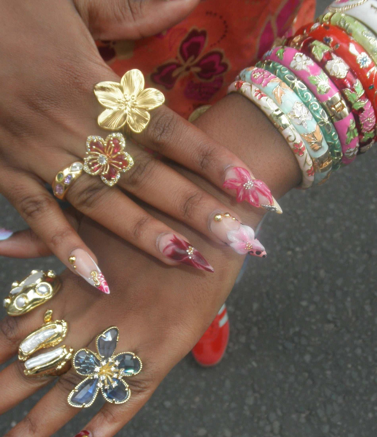 LOVELA RING IN ROSE RED, gold-tone floral rings with sparkling accents and colorful flower details on manicured fingers