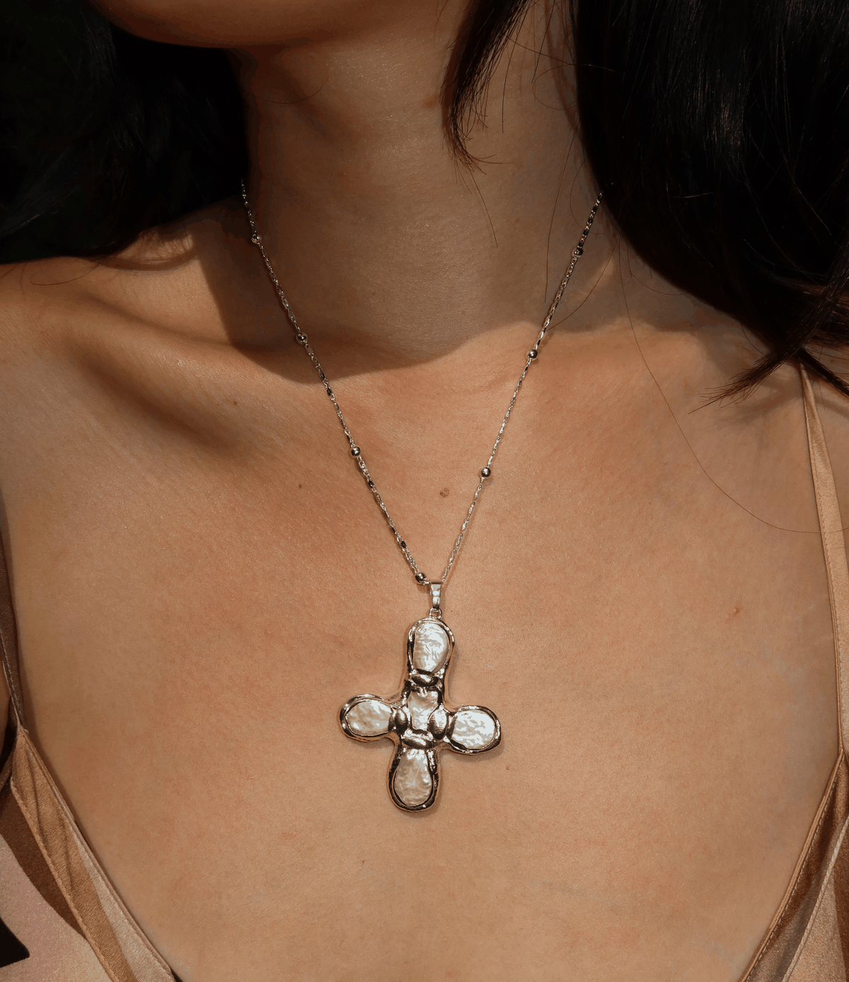 Olympia Necklace in silver-toned metal, featuring a fine chain and bold cross-shaped pendant with irregular details