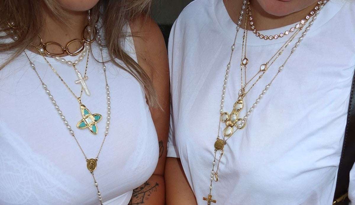 Your Ultimate Guide to Layering Jewellery, two white tops with layered gold necklaces, pendants and chains