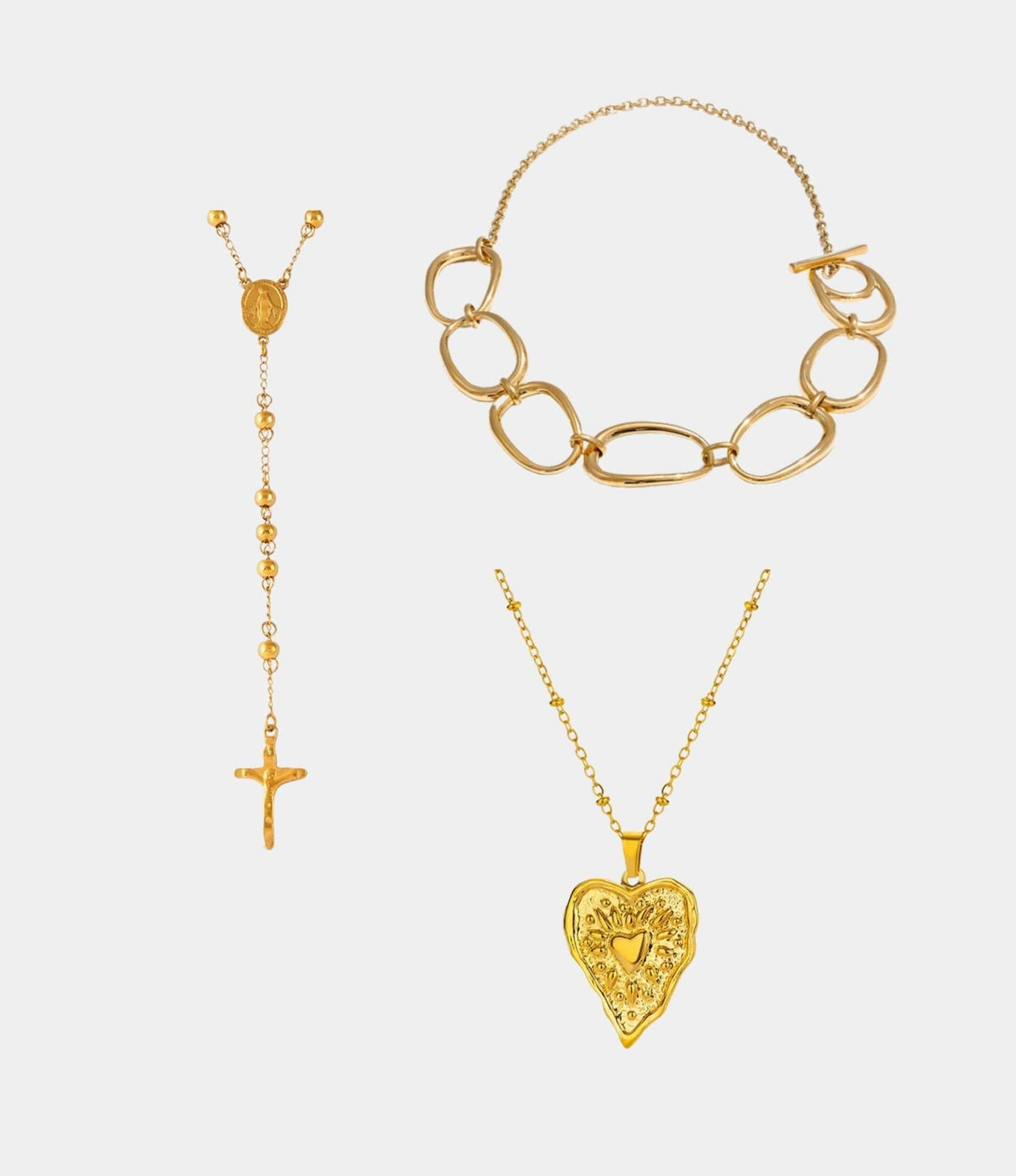 THE ICON NECKLACE SET features three gold-tone necklaces: oval links, a beaded cross pendant, and an ornate heart pendant.